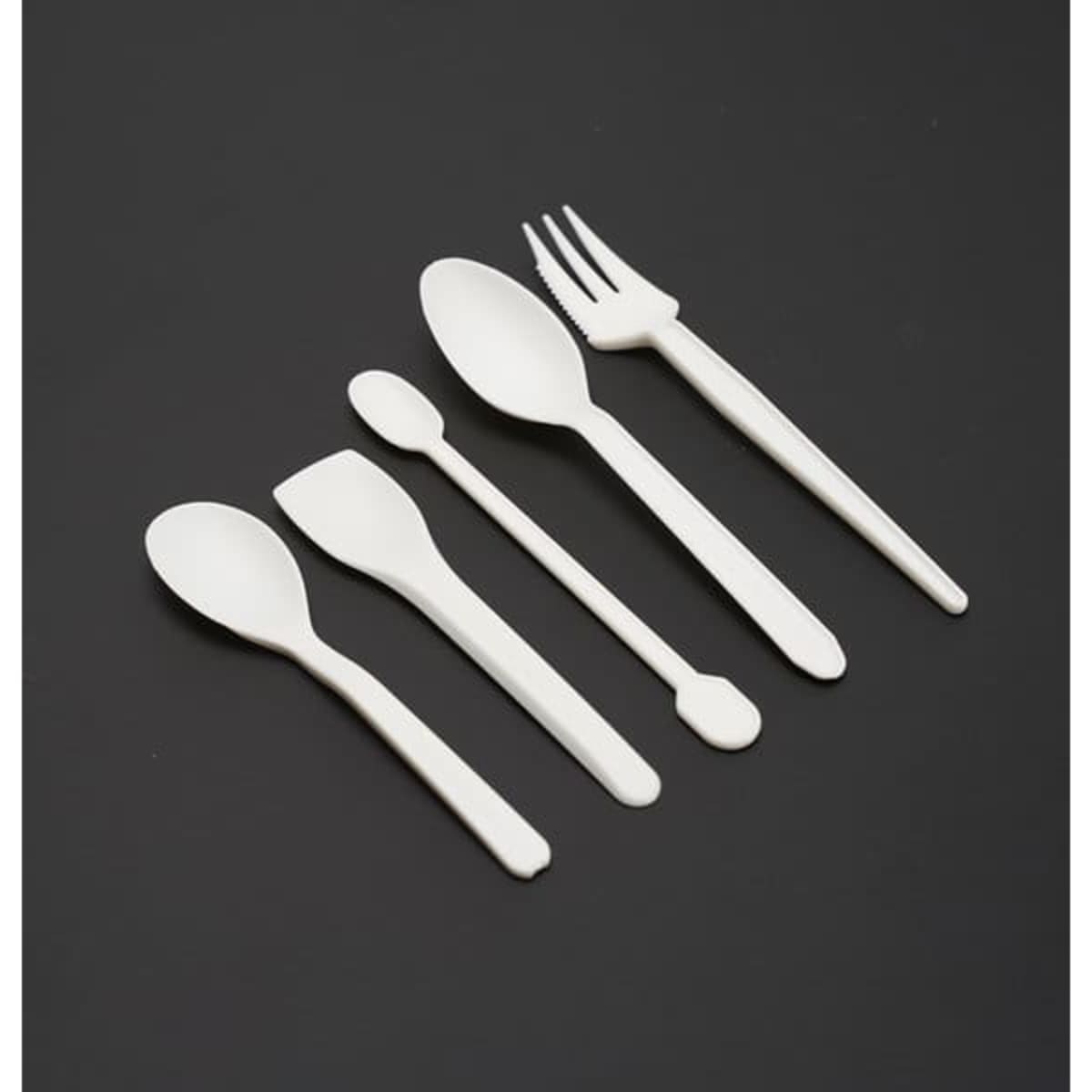 A set of five white PLA degradable dessert forks and spoons arranged on a dark background.