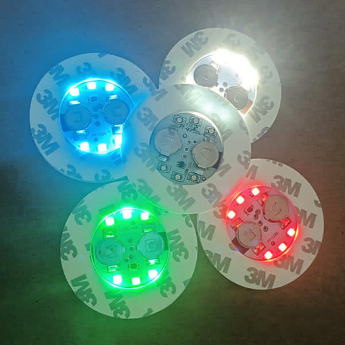 A set of illuminated LED coasters in various colours including blue, green, red, and white, each featuring a logo.