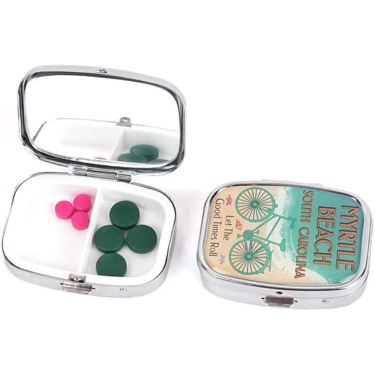 A portable metal pill box with a mirror, featuring green and pink pills, in a shiny silver finish.