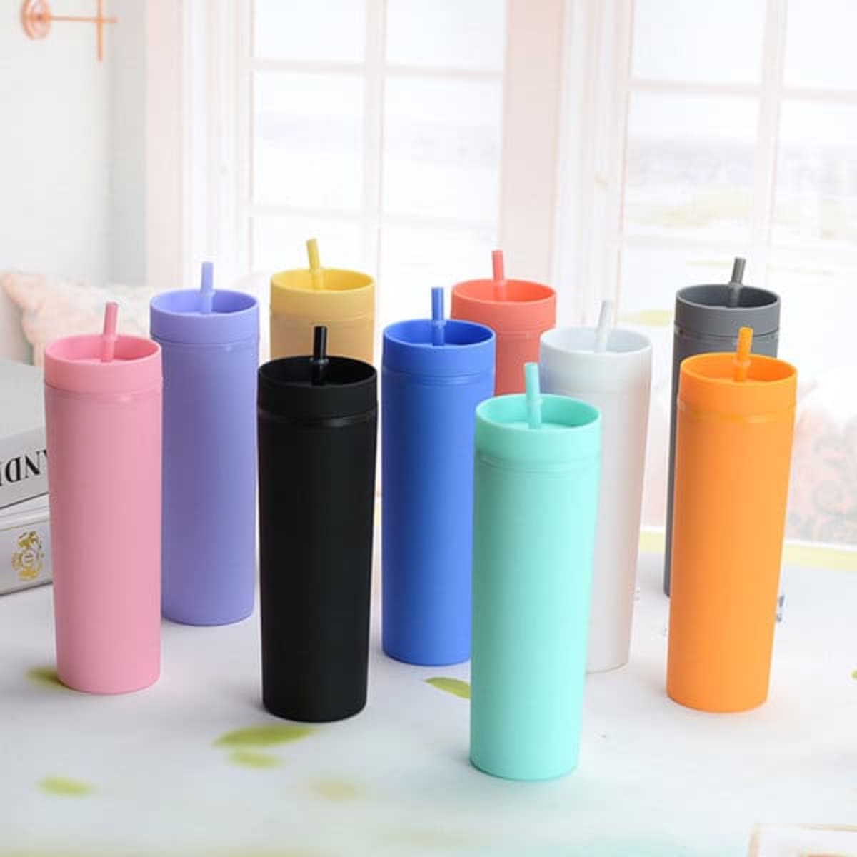 A group of ten 16 oz. double-layer frosted plastic cups in various colours, including pink, black, and mint green, with straws.
