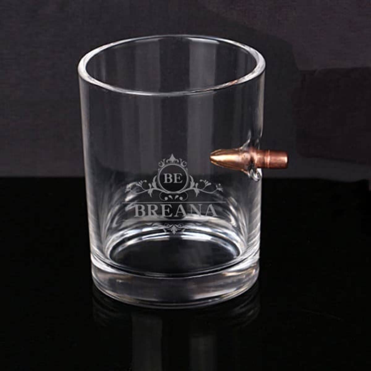 A clear whisky glass featuring a copper bullet design and a logo etched on the side.