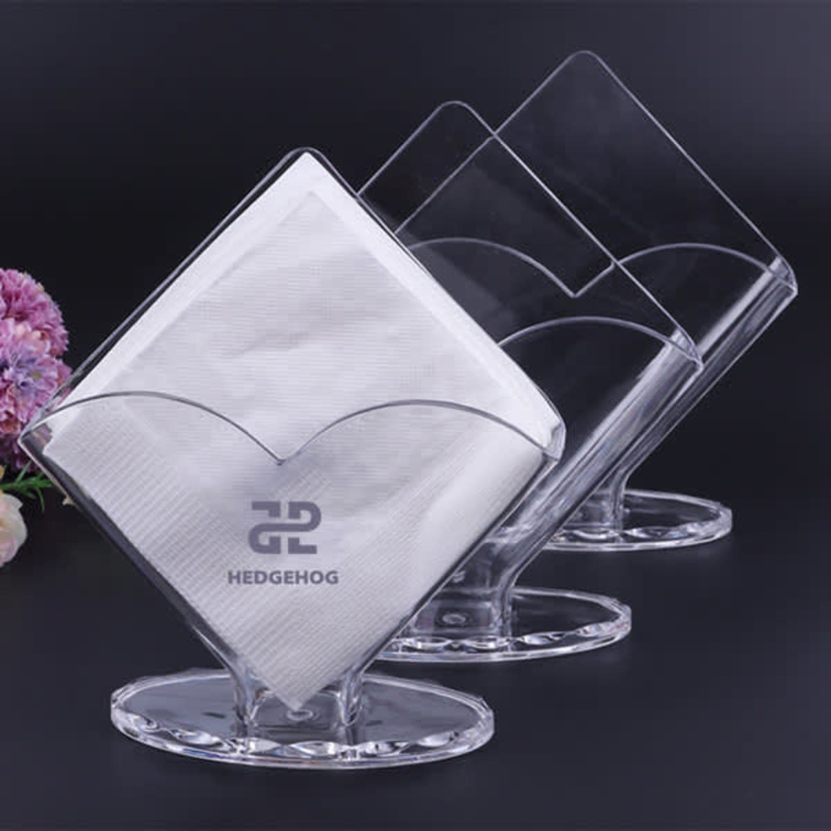 Acrylic vertical napkin holder in clear colour, displaying folded napkins with a logo on the front.