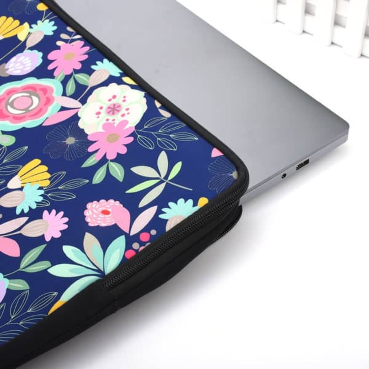 A zippered neoprene laptop sleeve with a floral pattern in vibrant colours, partially covering a silver laptop.