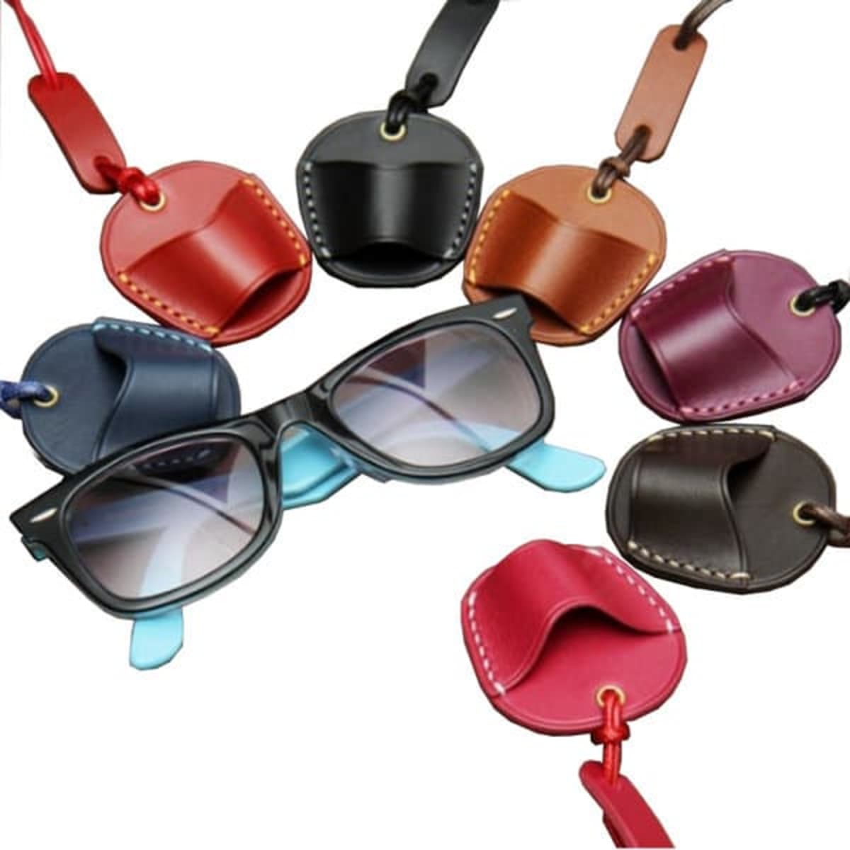 Leather glasses neck holders in various colours surround a pair of sunglasses. Each holder has a unique design and includes a logo.