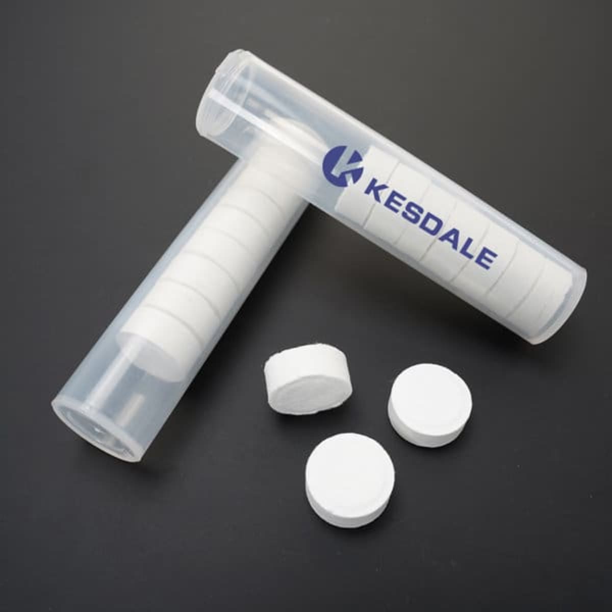 A clear tube containing compressed white face towels, with several towels outside the tube. The tube has a logo.
