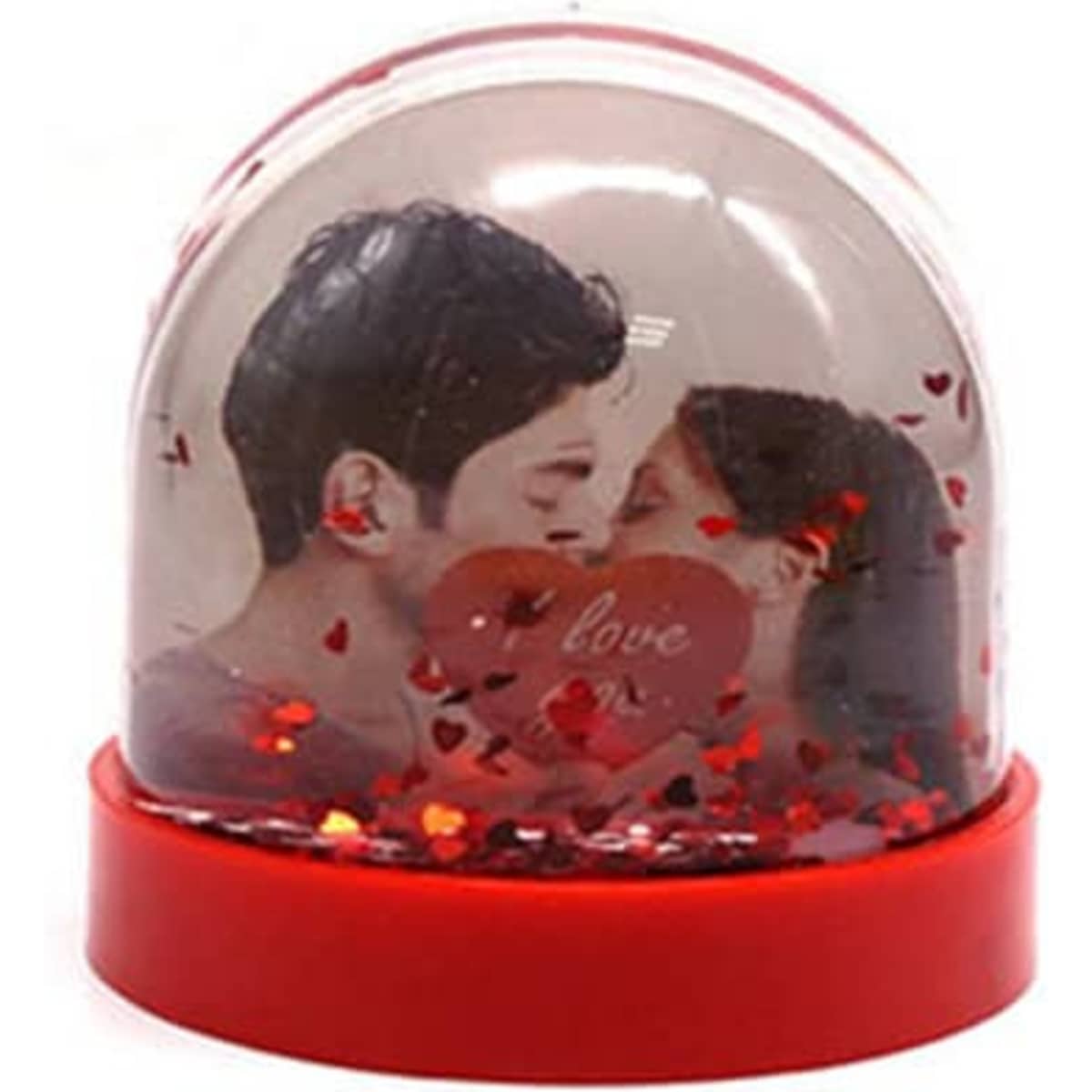 A snow globe featuring a romantic photo insert, filled with red hearts and glimmering confetti, set in a red base.