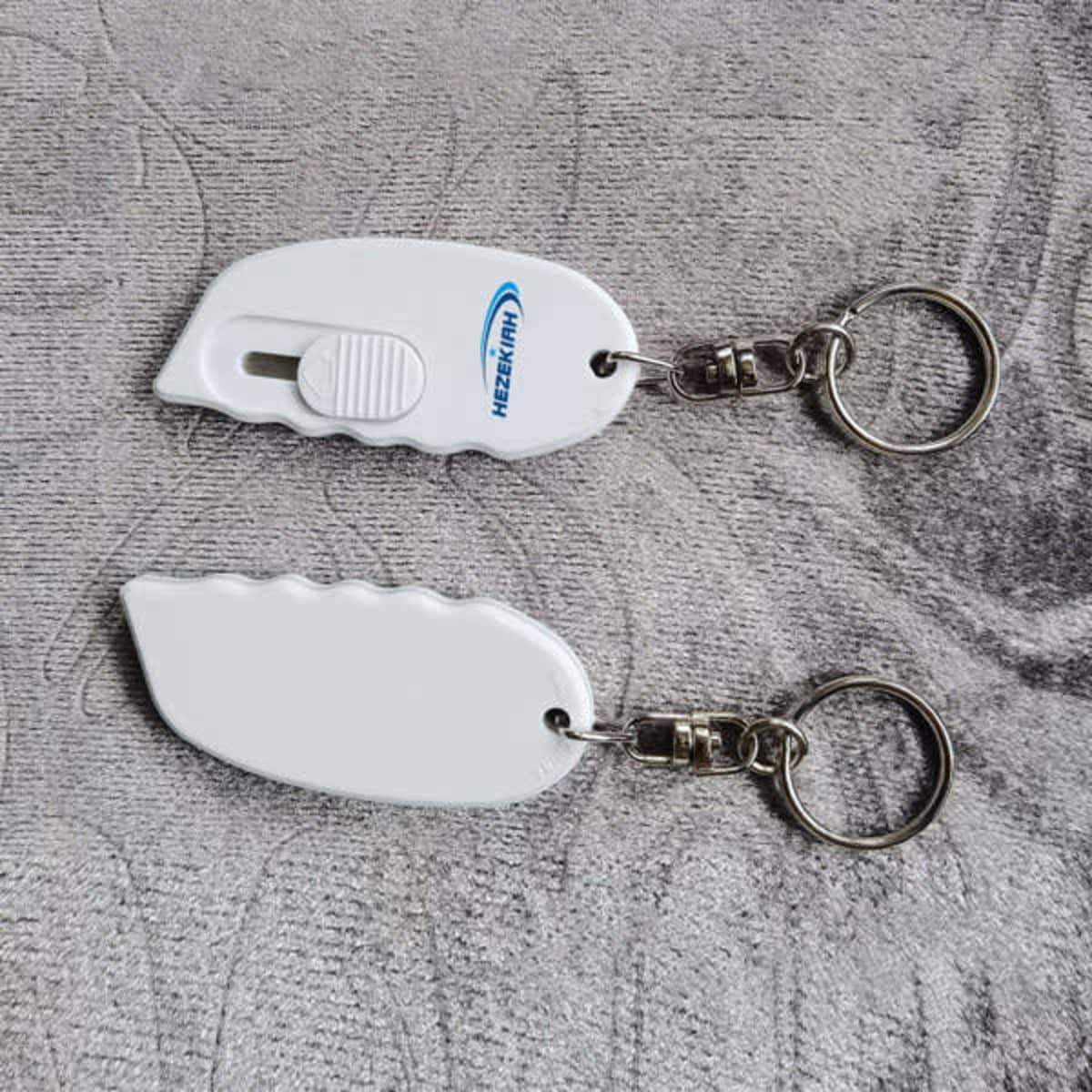 A white mini plastic safety box cutter with a keychain attachment, featuring a smooth design and a metal keyring.