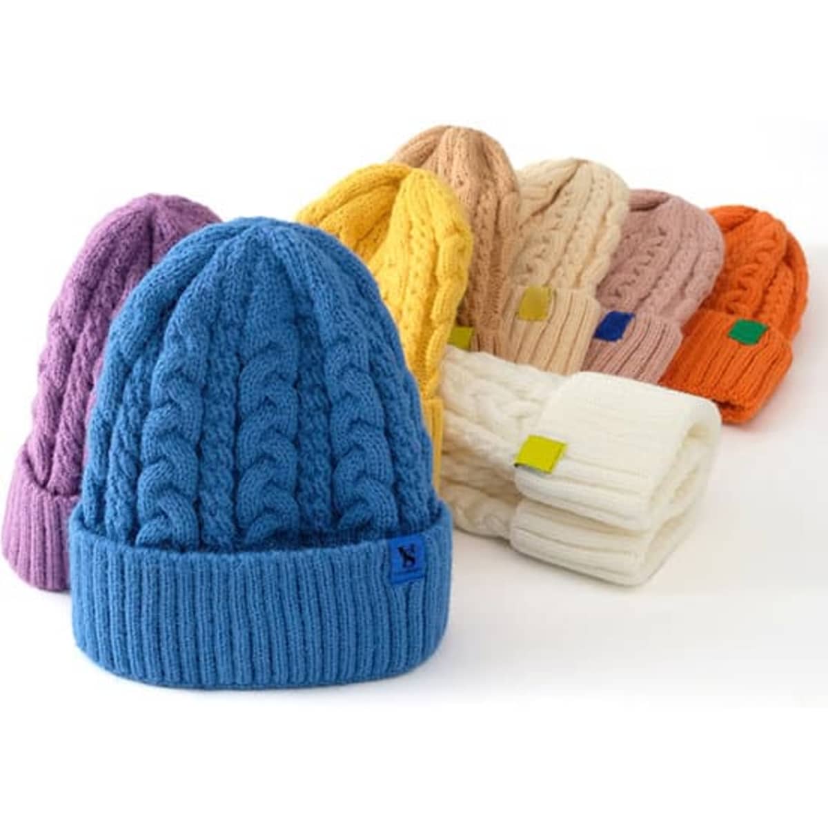 A collection of vibrant adult cable knit beanies in blue, purple, yellow, pink, orange, and cream, featuring various logos.