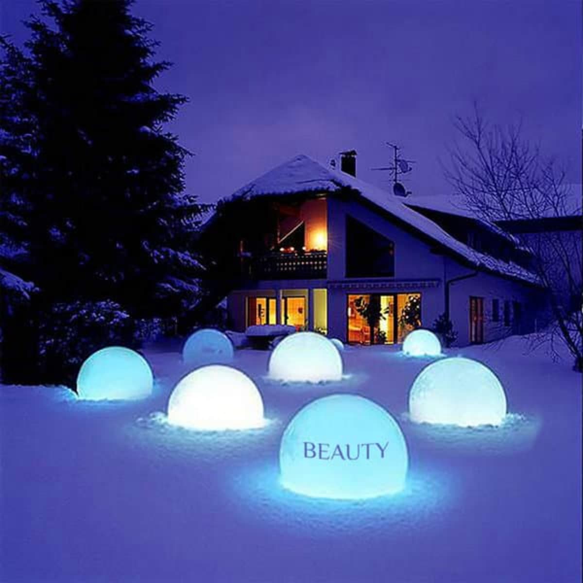 A set of glowing blue luminous balloons in a snowy landscape near a house at night.