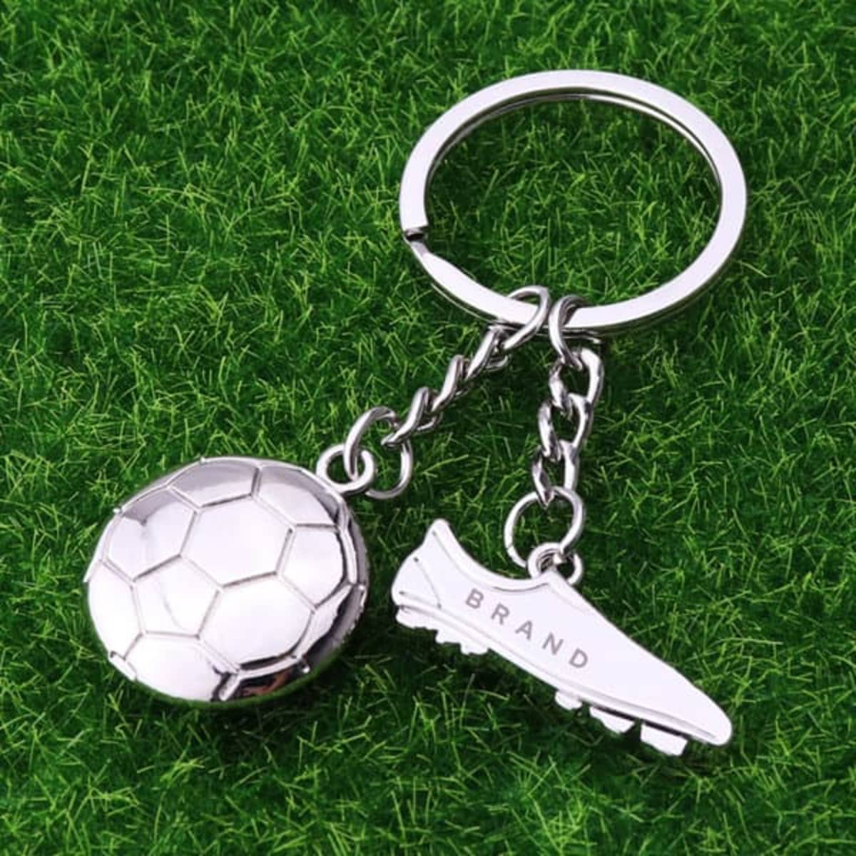 A silver football charm keychain with a soccer ball and a boot, featuring a branding logo.