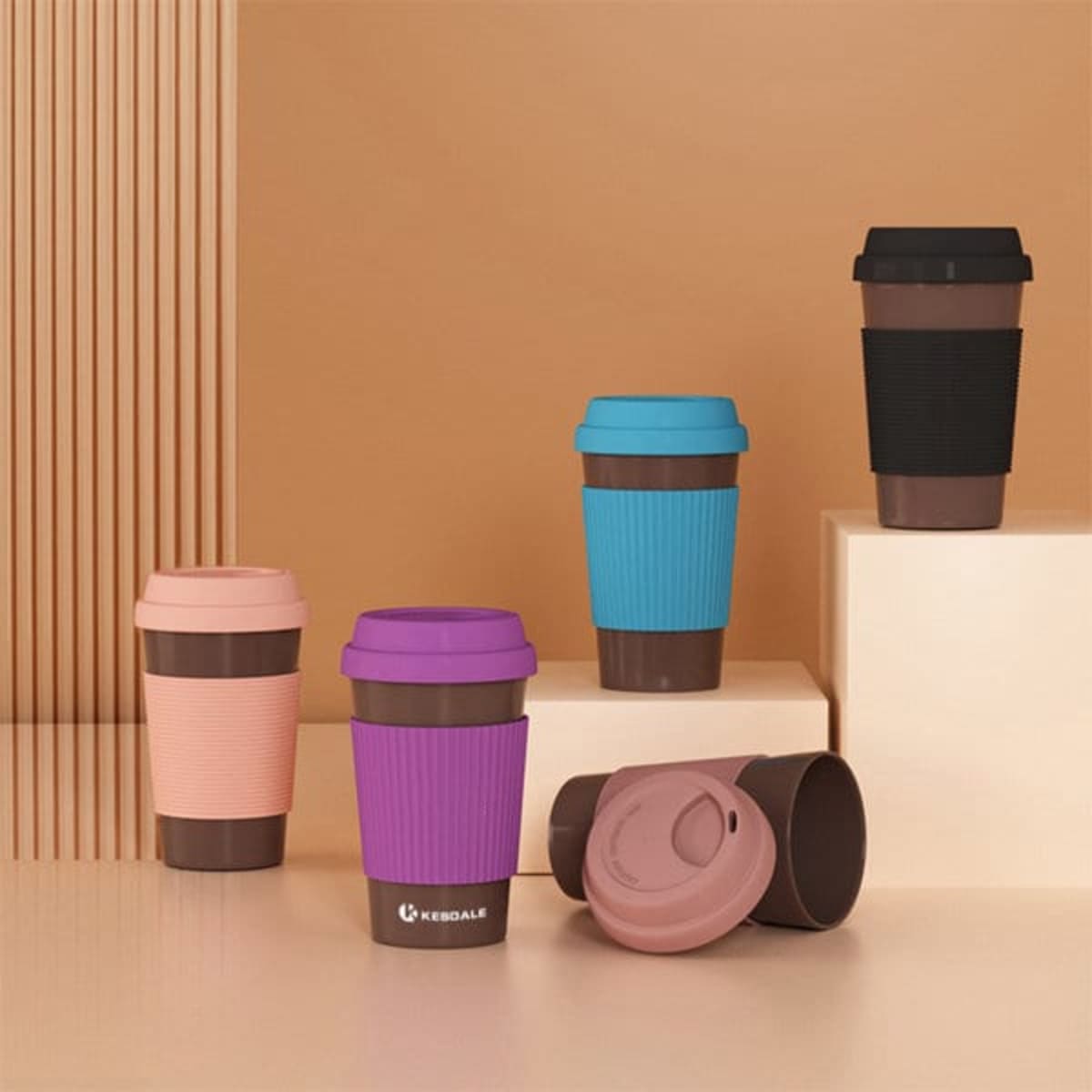 A set of eco-friendly coffee mugs in pink, blue, purple, and black with silicone grips and lids.