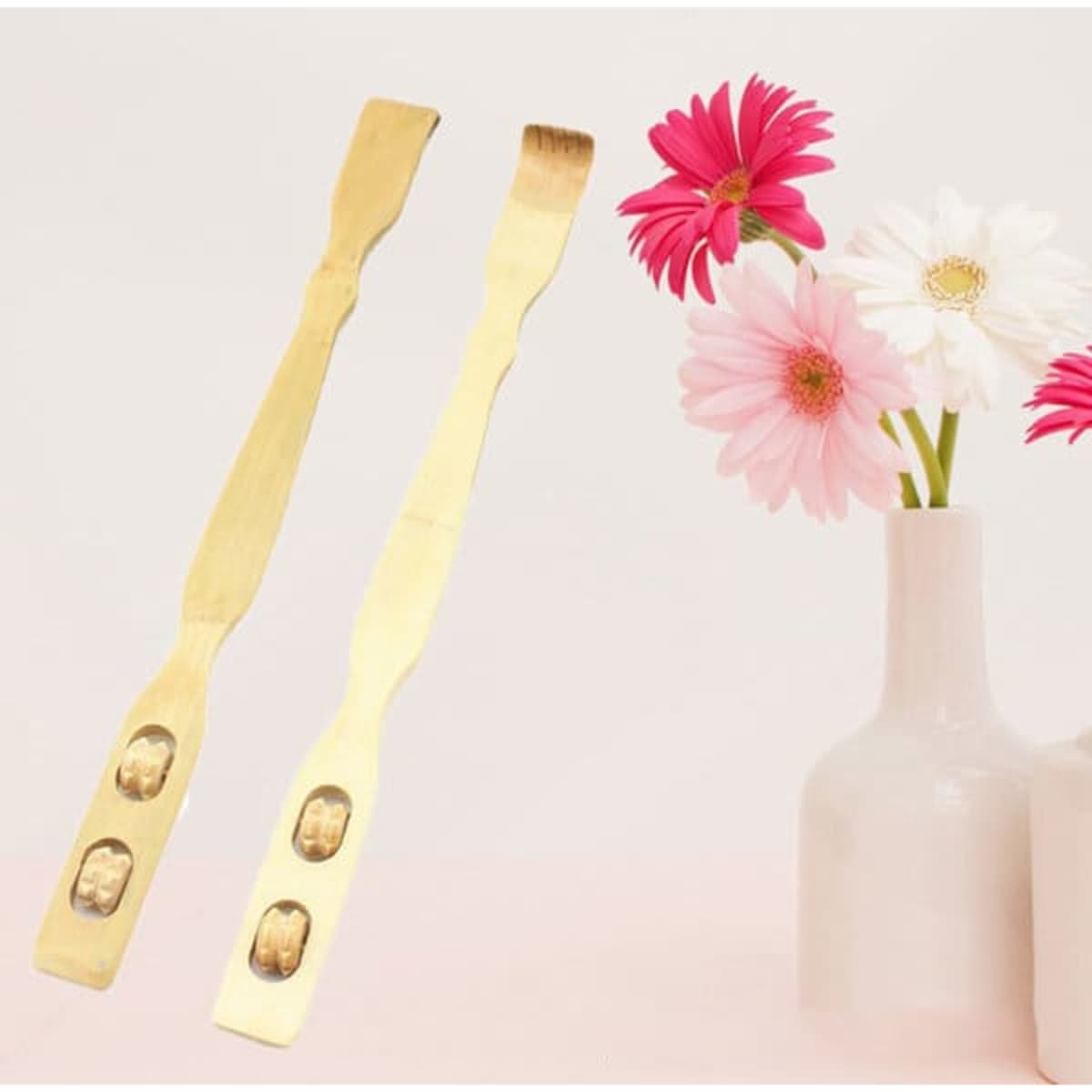 A bamboo back scratcher with massage rollers, featuring a natural finish and two ergonomic ends, beside a vase with flowers.