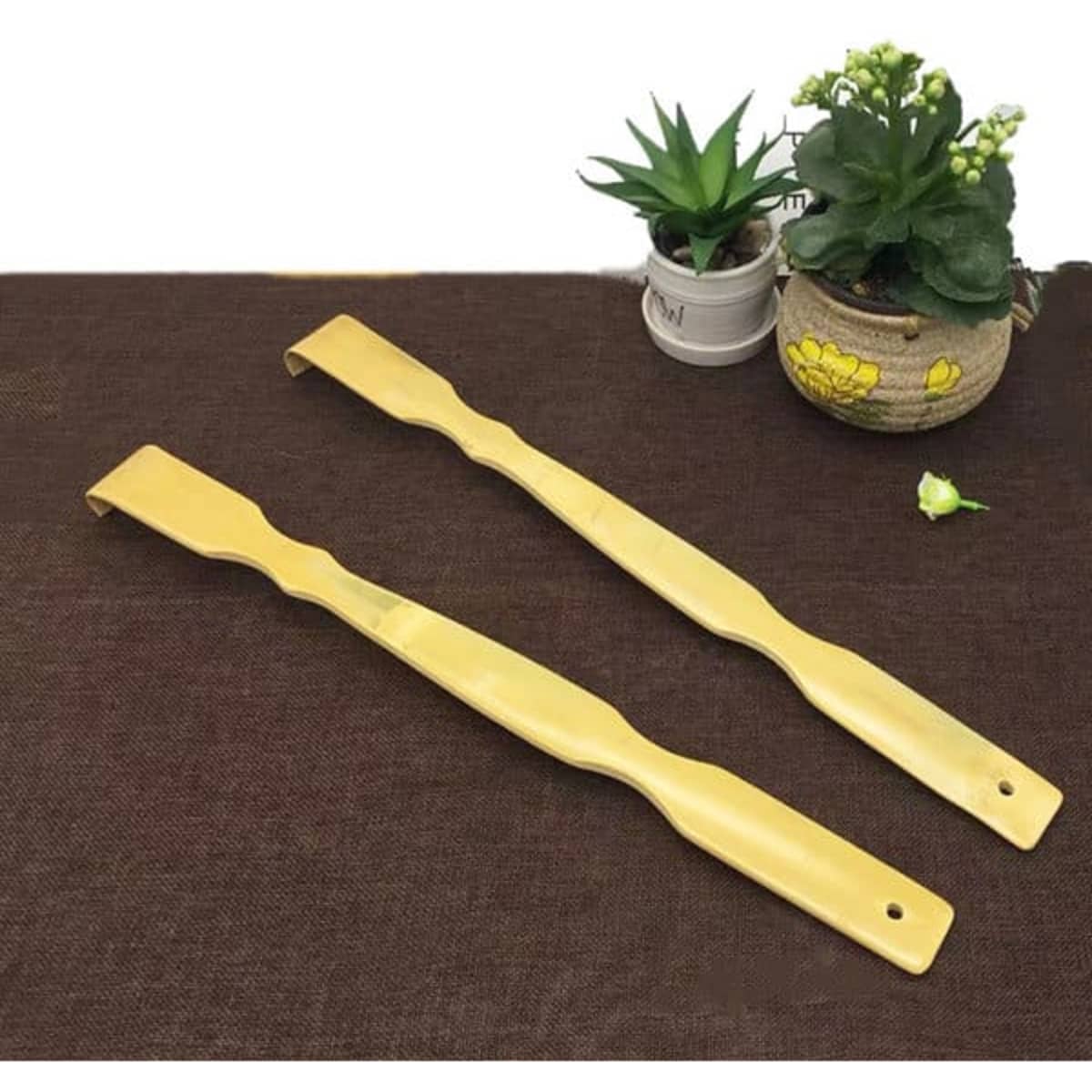 A bamboo back scratcher in a light yellow colour, featuring a curved design, placed on a brown surface with small plants.