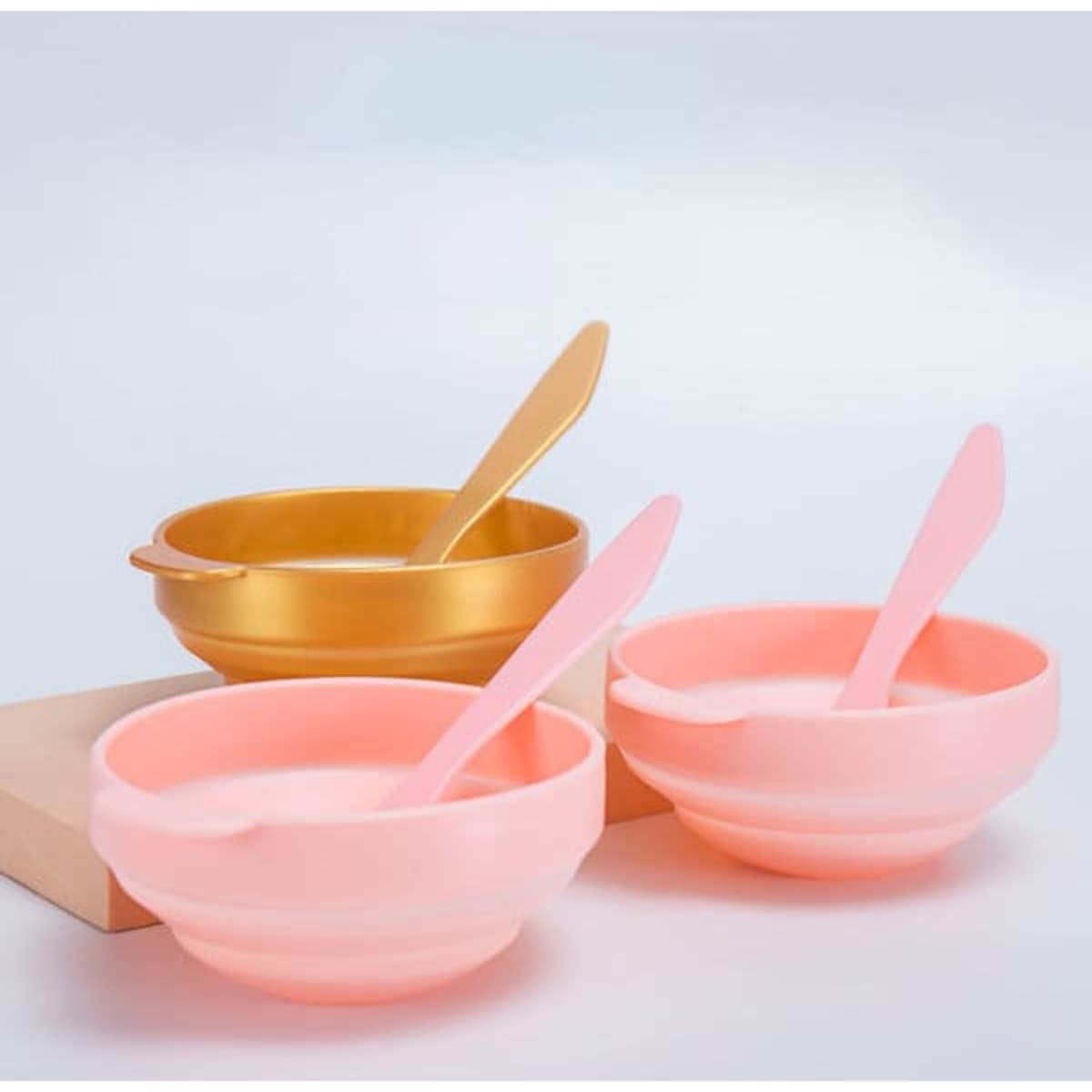 A set of three bowls in pink and gold, each with a matching spoon, displayed on a light background.