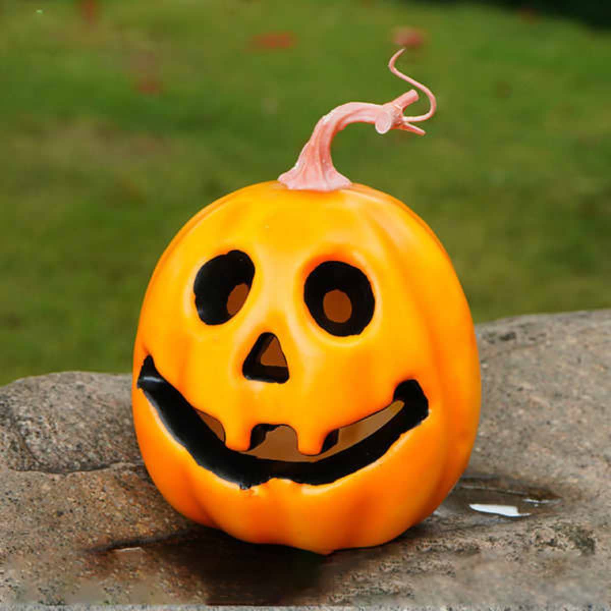 A bright orange pumpkin with a ghost face, featuring black eyes, a smiling mouth, and a pink stem.