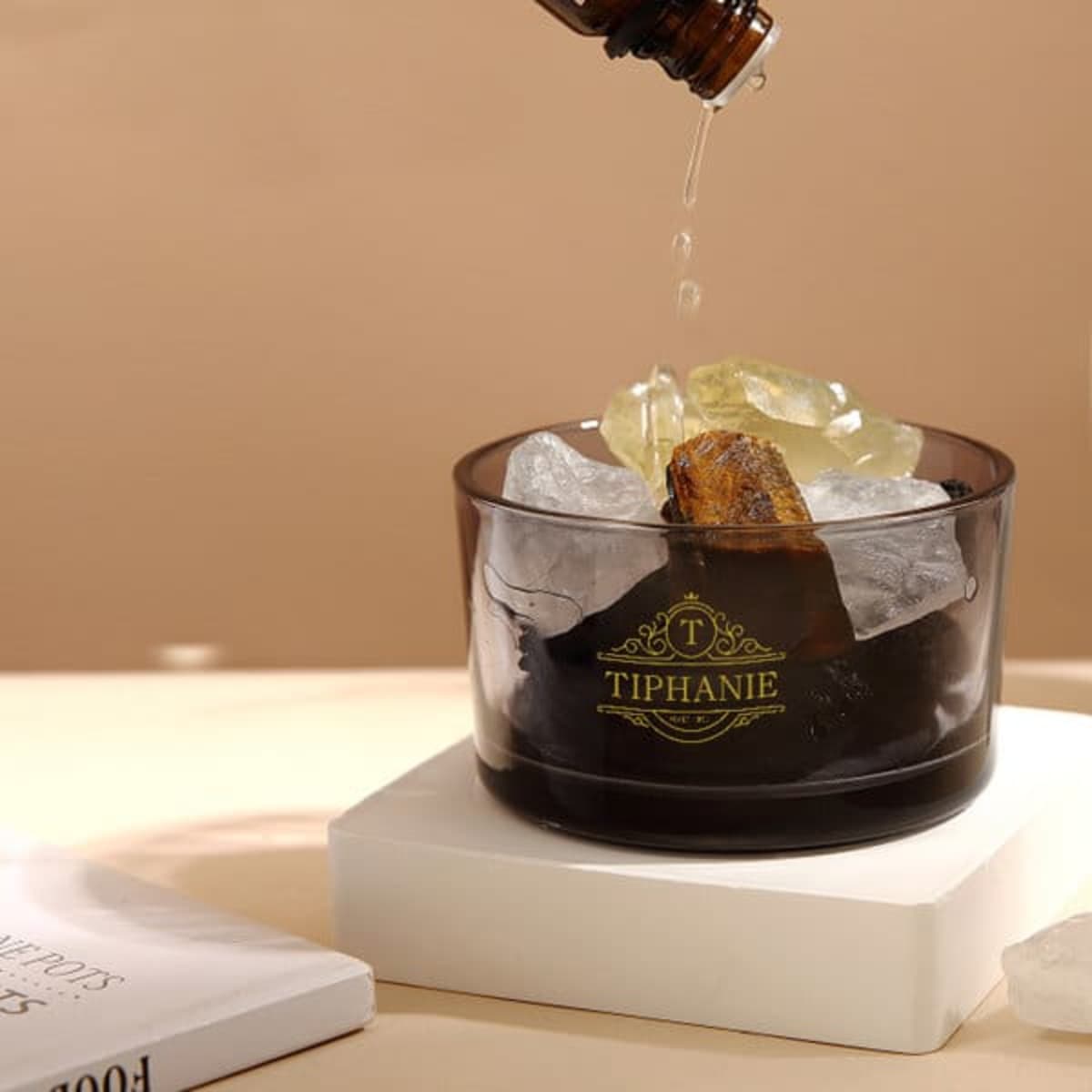 A black glass essential oil diffuser filled with stones and drops of oil, resting on a white base.