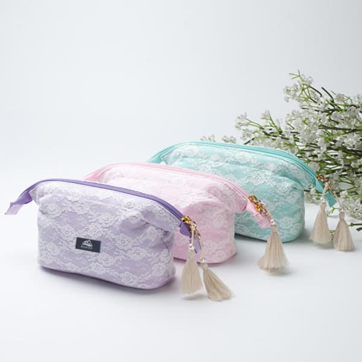 A lace cosmetic bag set in lavender, pink, and mint green, featuring tassel zippers and a logo.