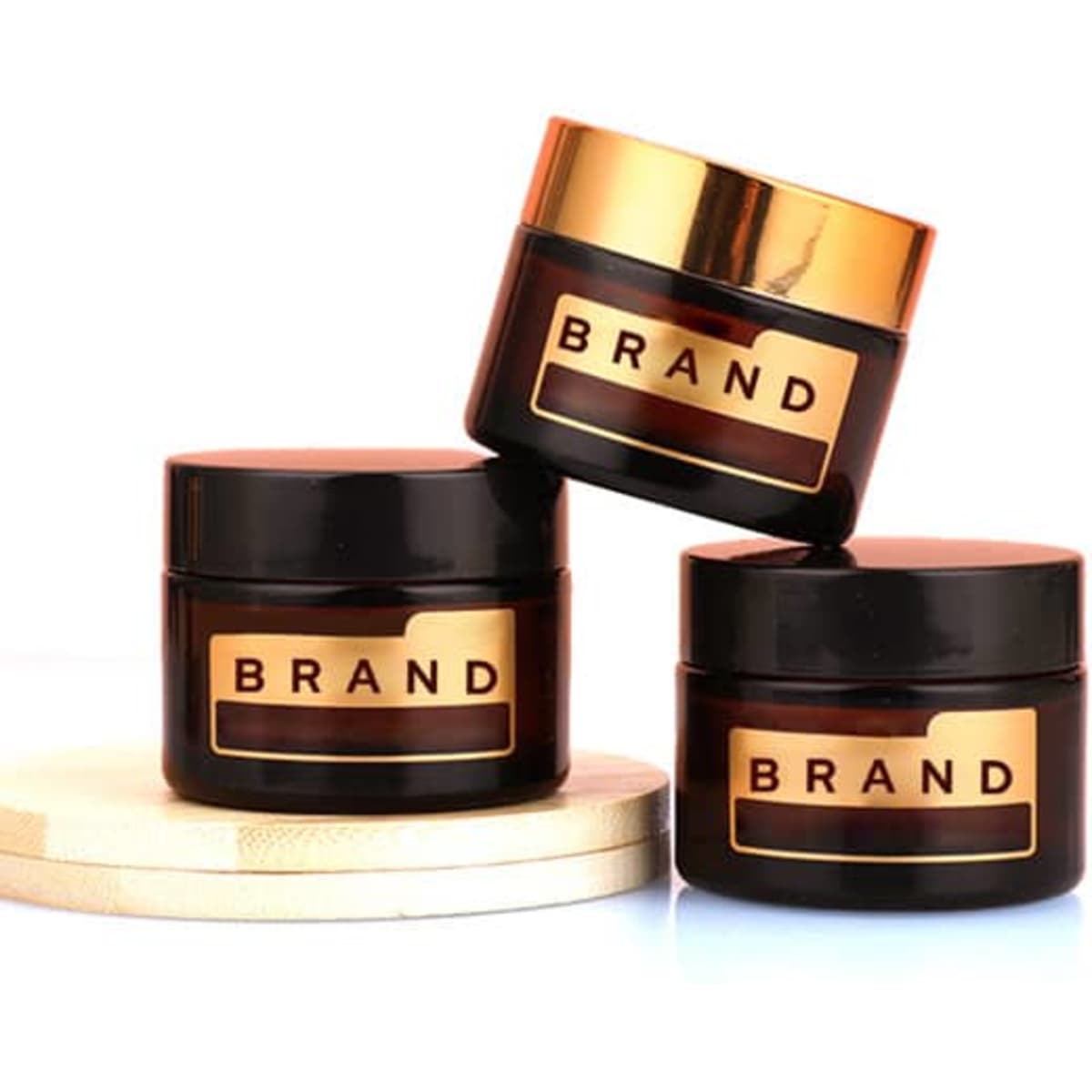 Three round, dark brown cosmetic jars with gold lids, featuring branding labels. Set on a wooden surface.