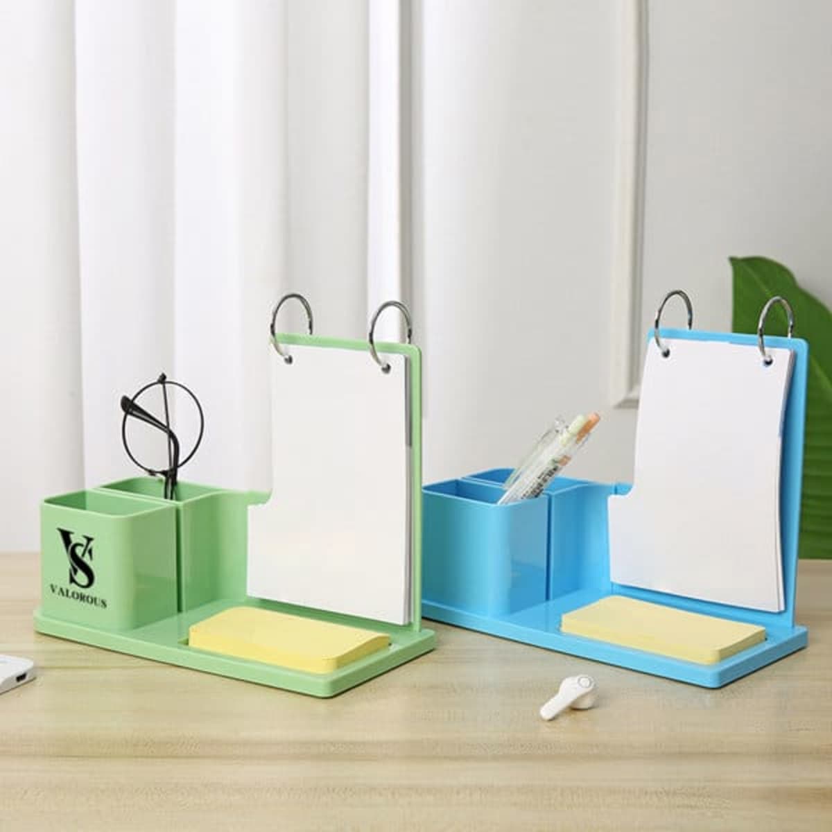 A desk pen holder in green and blue with compartments for pens, sticky notes, and a calendar pad, featuring a logo.