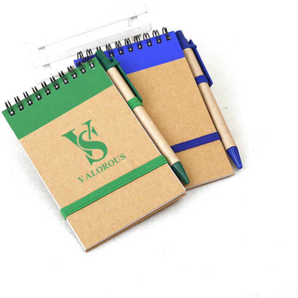 A kraft paper spiral notebook in green and blue, each with a matching pen and an elastic band holder.