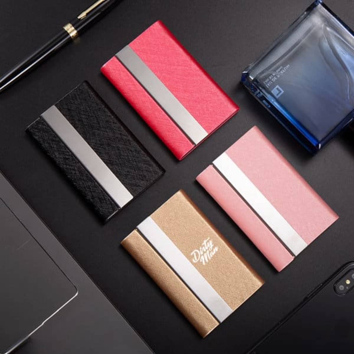 A set of four PU leather business card cases in black, pink, gold, and red, featuring metal accents.