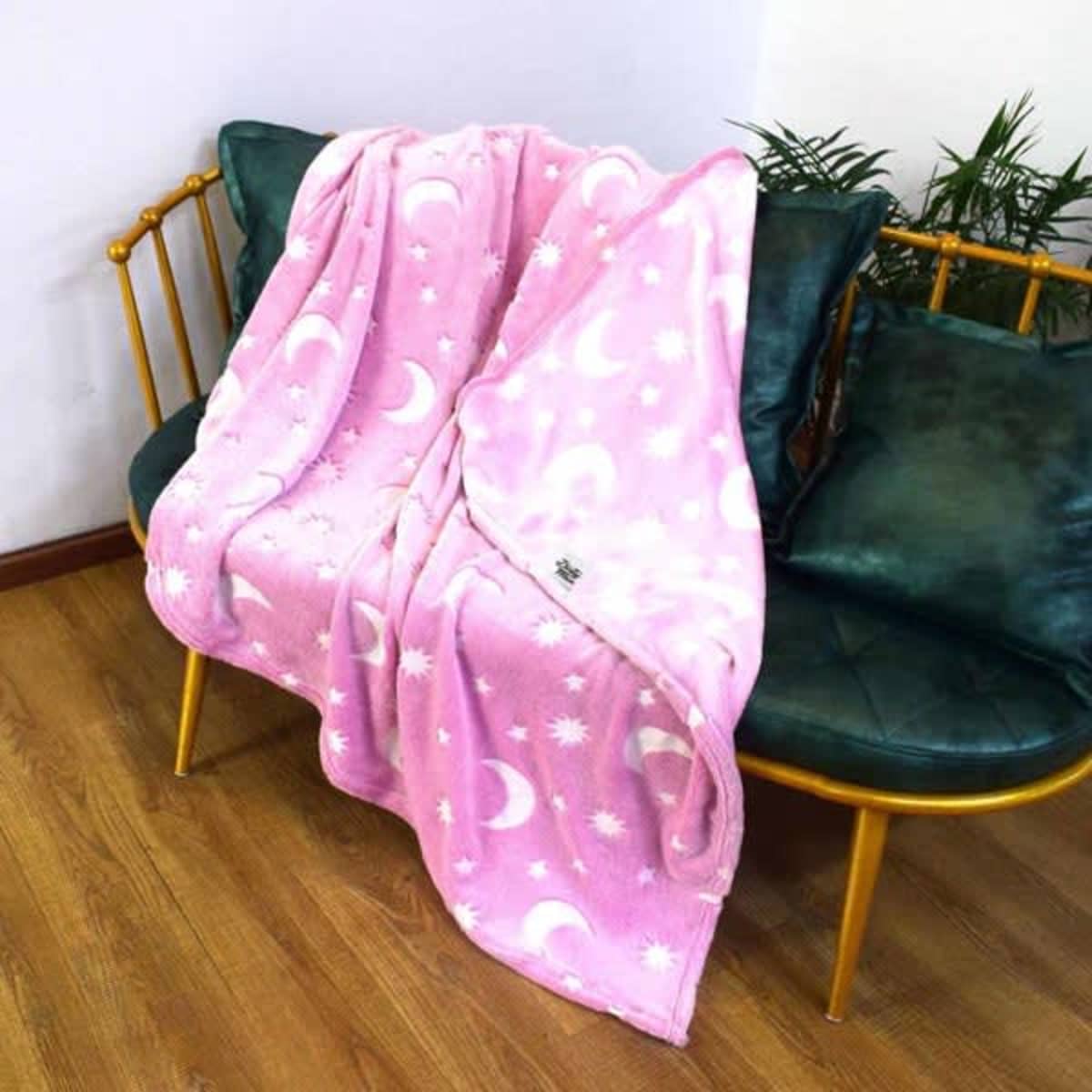 A pink glow-in-the-dark blanket featuring moon and star patterns, draped over a green sofa.