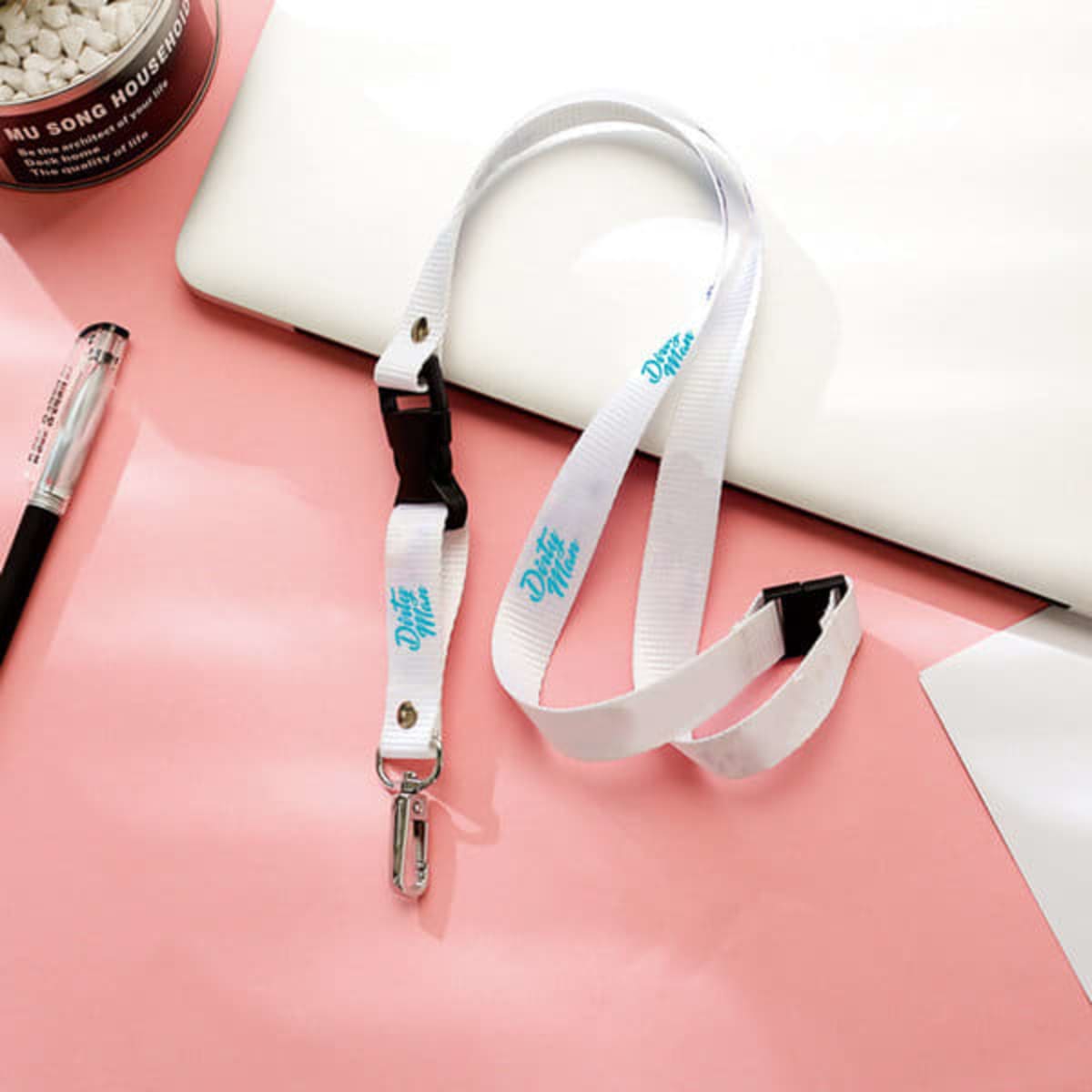 A white lanyard with a buckle and a metal clasp, resting on a pink surface alongside a pen and notebook.