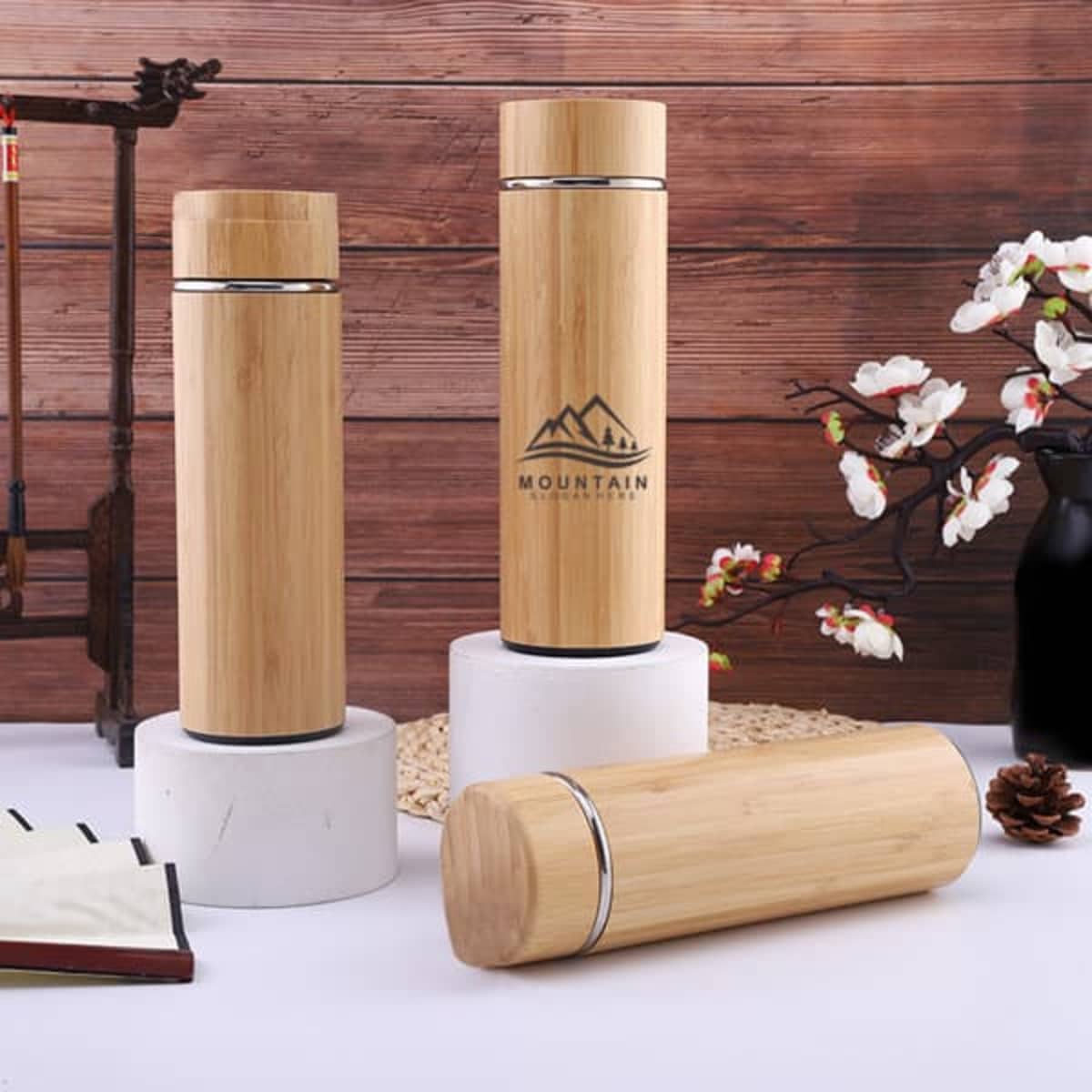 A drink bottle made of bamboo with a sleek design, featuring a logo and placed on a marble stand.