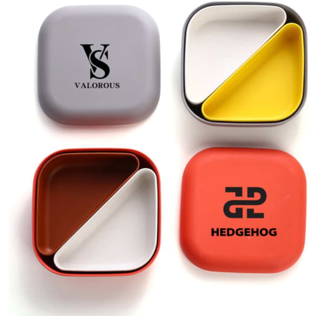 A set of four bento lunch boxes in grey, yellow, brown, and red, featuring logos on two of the boxes.