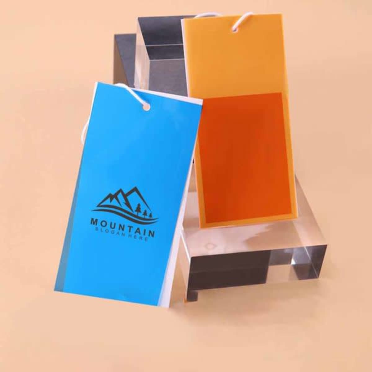 Two custom PVC hang tags in blue and orange, displayed on a clear block. One tag features a logo.