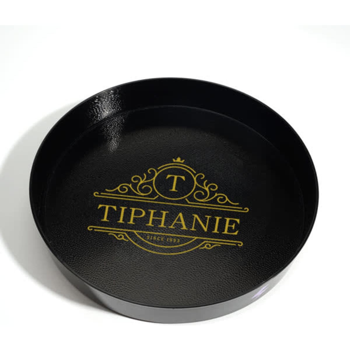 A round, black non-slip tray featuring a decorative logo in gold.