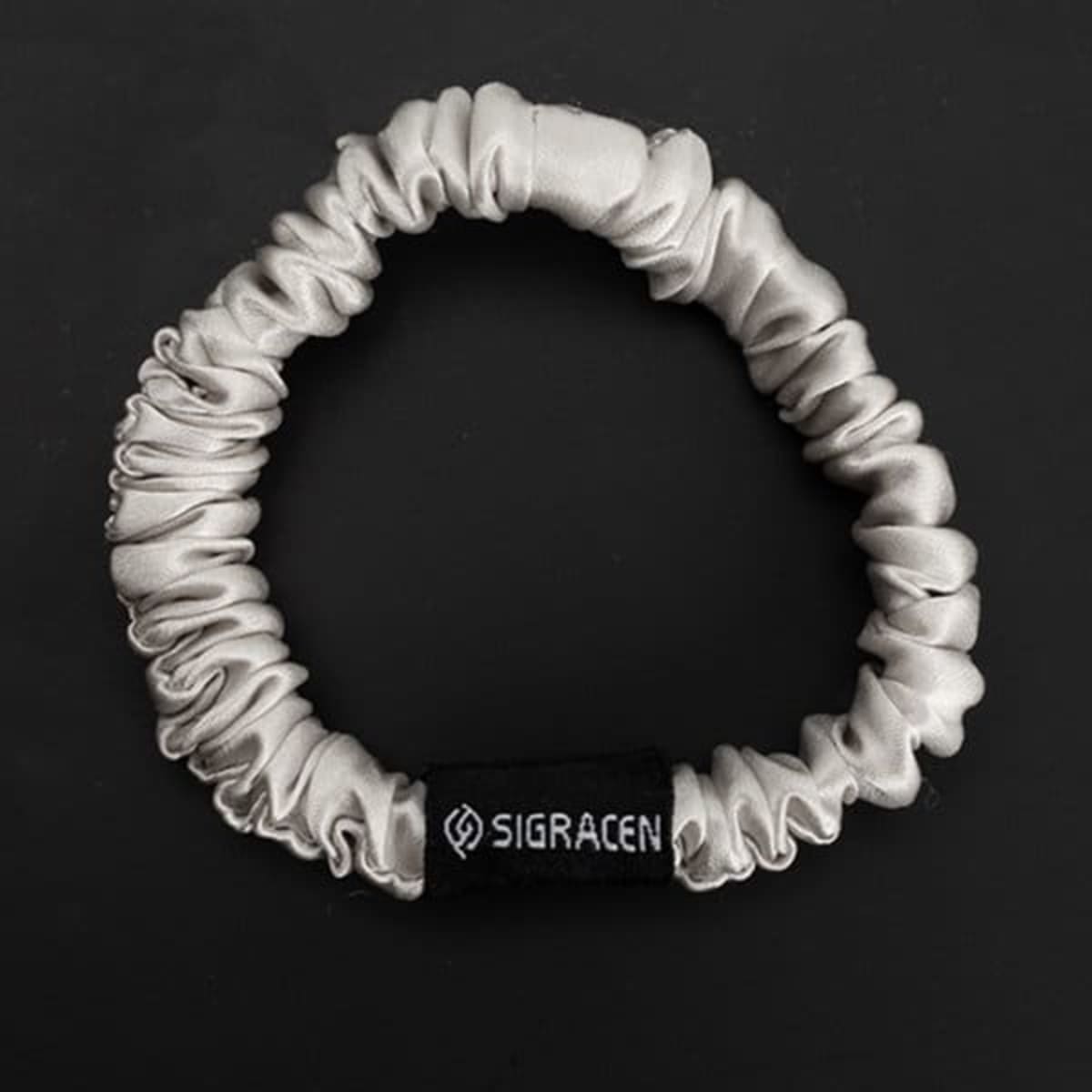 A silky, light grey scrunchie made from 100% Mulberry silk, featuring a brand logo.