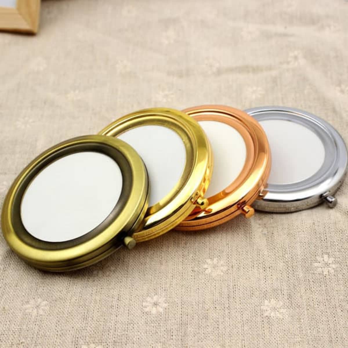A round pocket double-sided makeup mirror in gold, silver, copper, and bronze finishes, showcasing a sleek design with a logo.