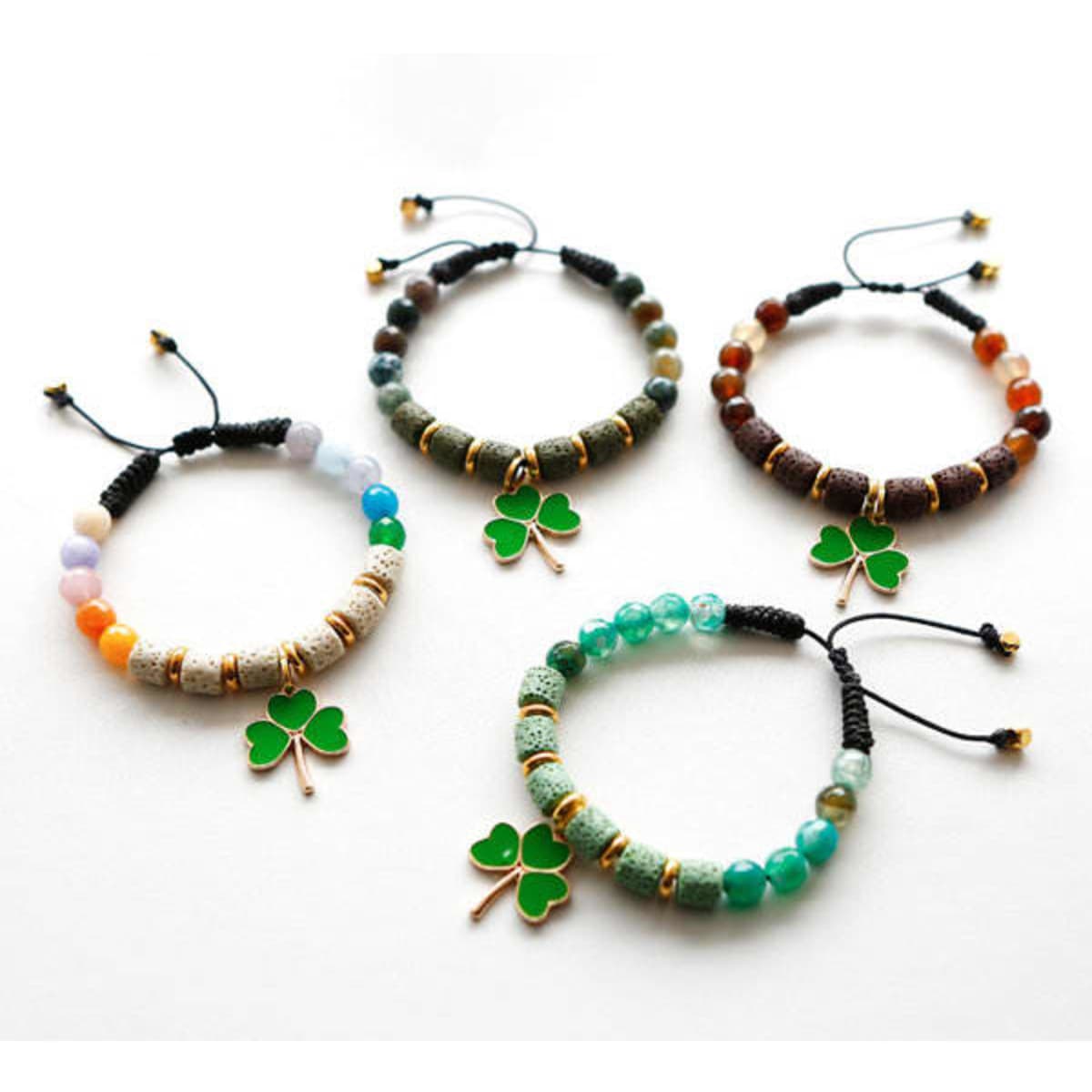Four colourful beaded bracelets featuring clover charms, including shades of green, orange, and brown. Each has a unique design.