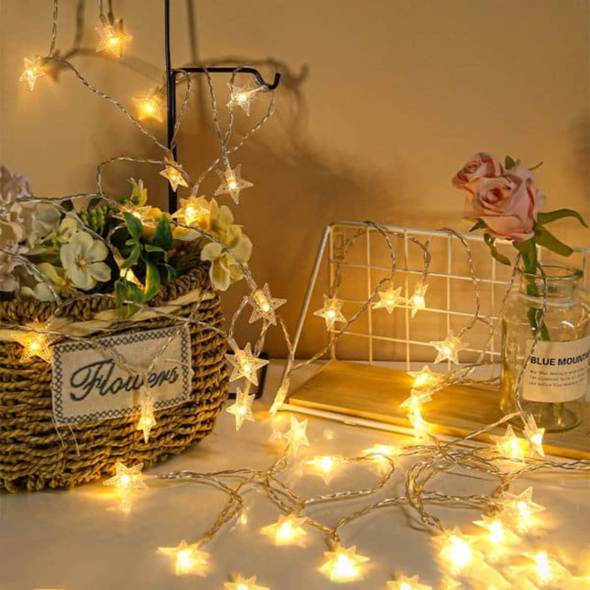A decorative string of LED star lights in warm white, intertwined with flowers and a glass jar.