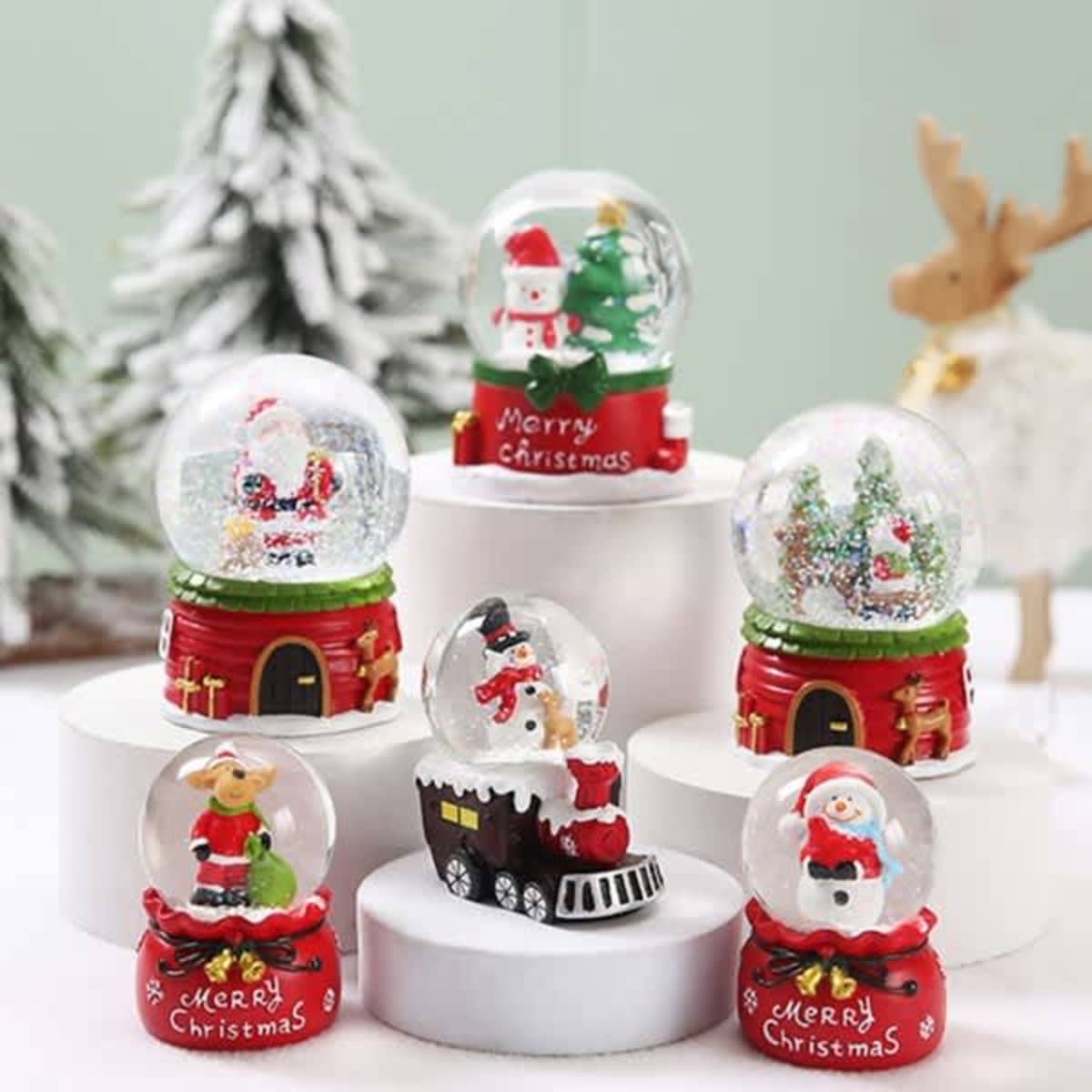 A collection of six colourful Christmas snow globes featuring festive scenes and characters on white pedestals.