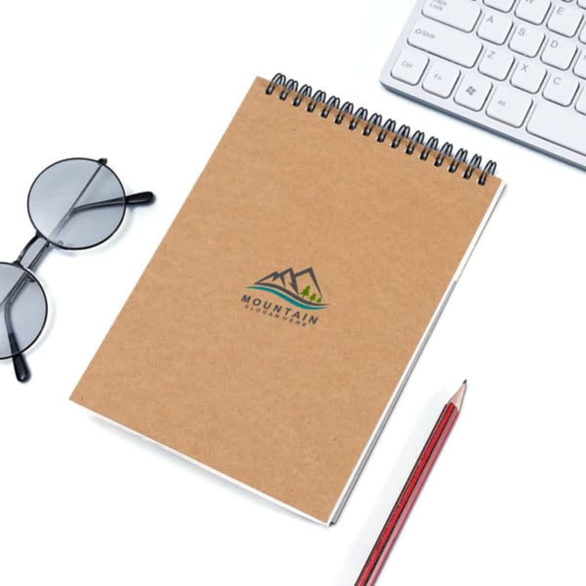 A4 top spiral bound sketch book in brown with a logo, accompanied by a pencil, glasses, and a keyboard.
