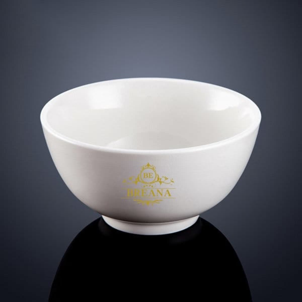 A white melamine salad bowl with a rounded shape and a gold logo at the base, set against a dark background.