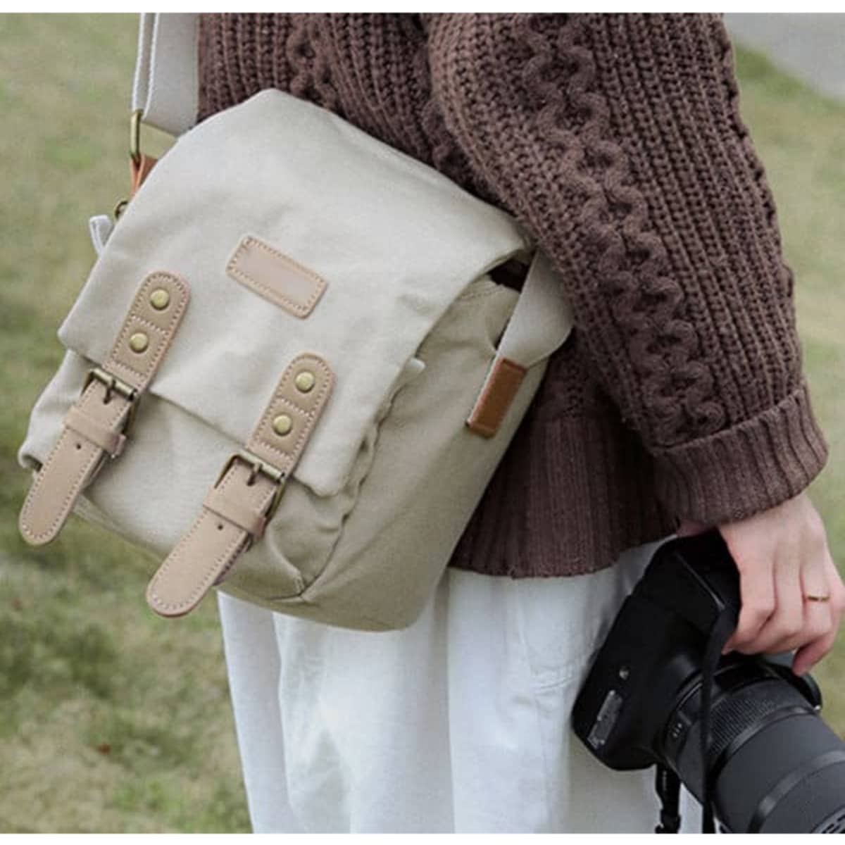 A classic vintage camera bag in beige with leather accents, worn over a brown, knitted sweater.