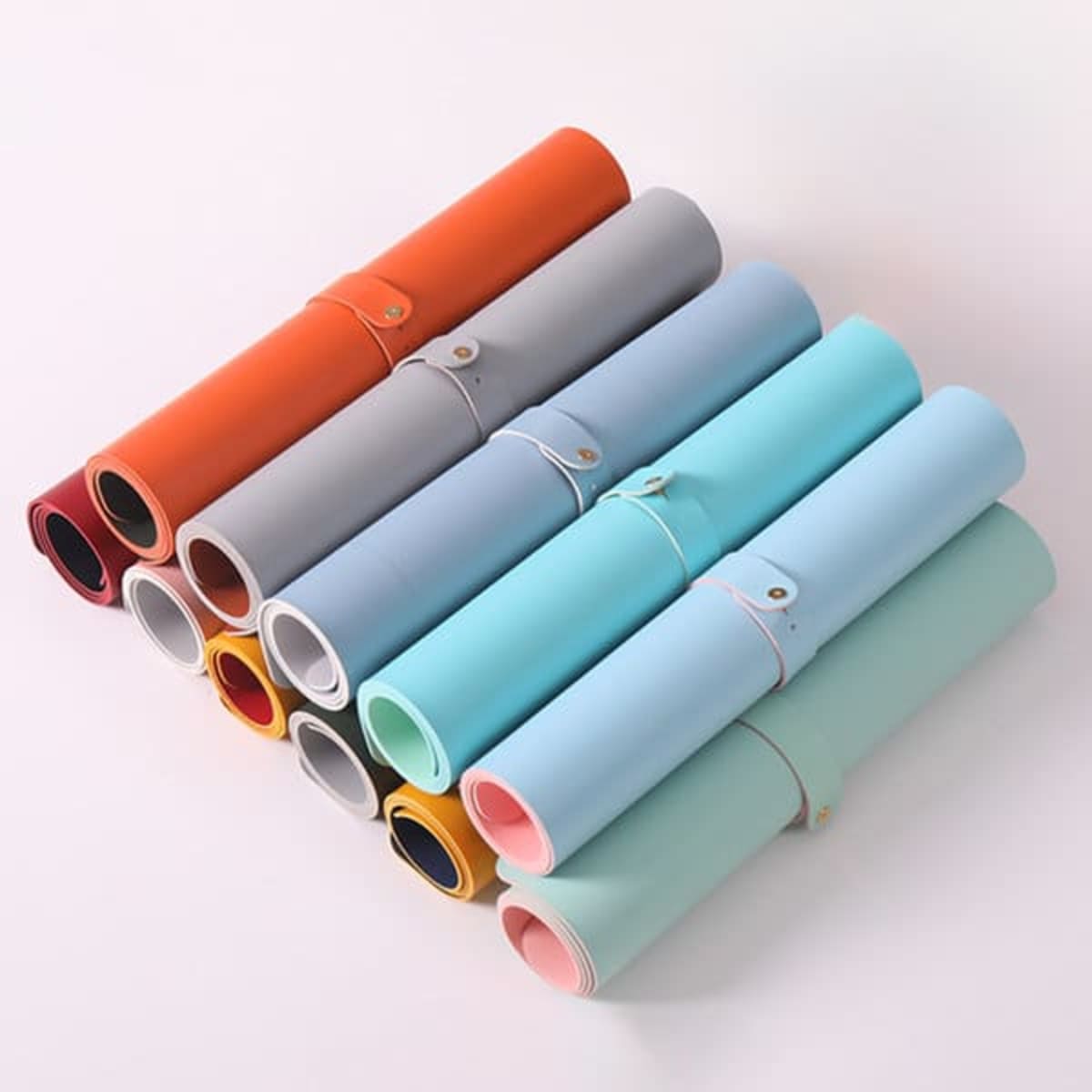 Multiple rolled desk mats in various colours, including grey, orange, blue, and mint, secured with bands.