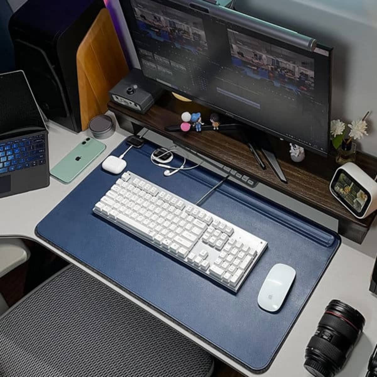 A navy PVC leather desk mat featuring a magnetic cable holder, with a keyboard, mouse, and camera on a desk.
