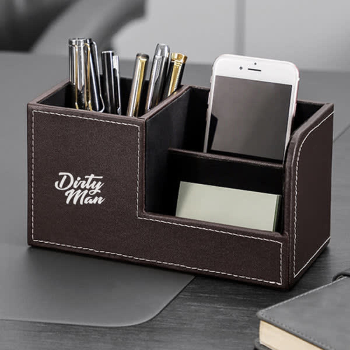 A brown leather desktop pen storage holder with compartments for pens, a smartphone, and sticky notes.