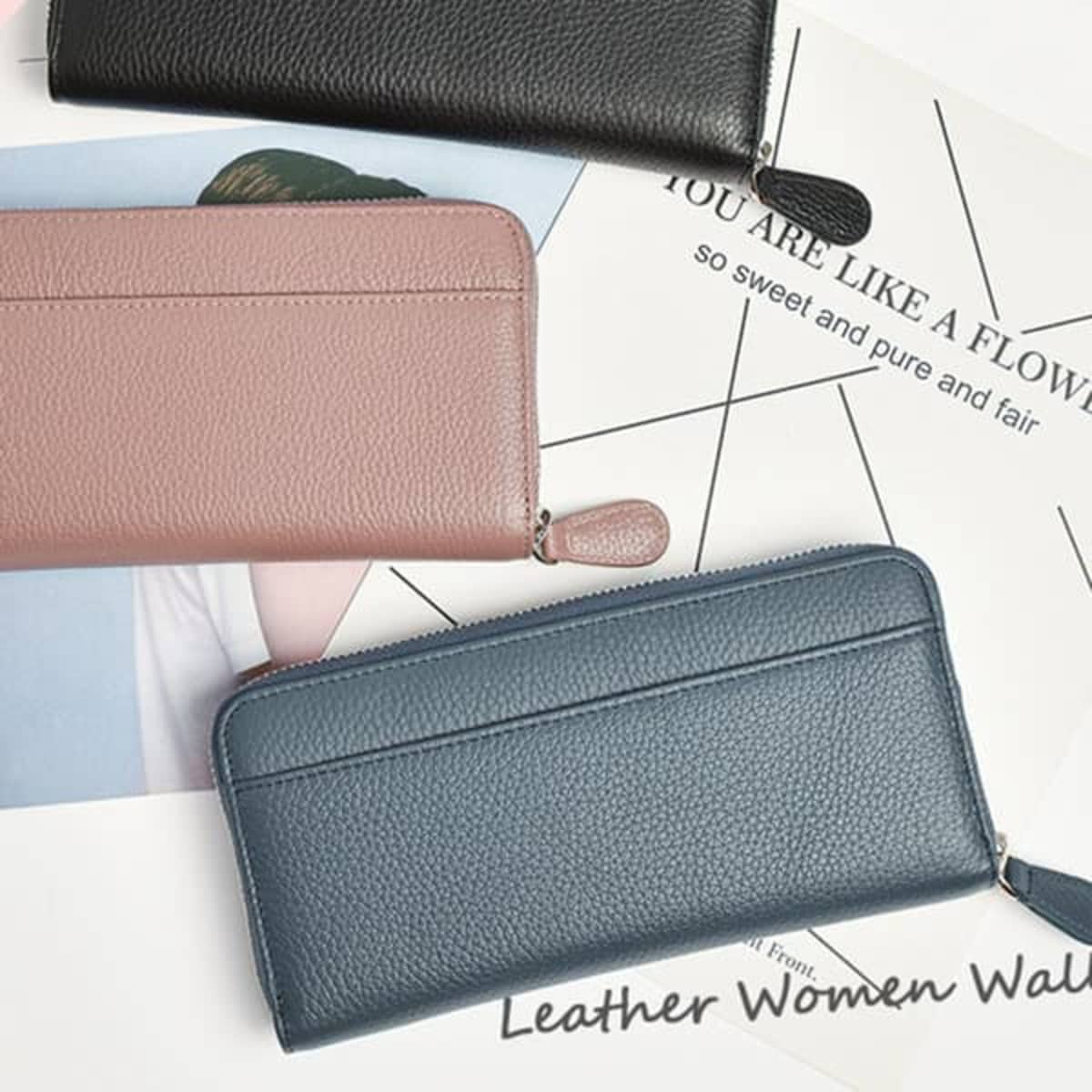 Three leather wallets in black, pink, and blue arranged on a flat surface with some printed materials underneath.