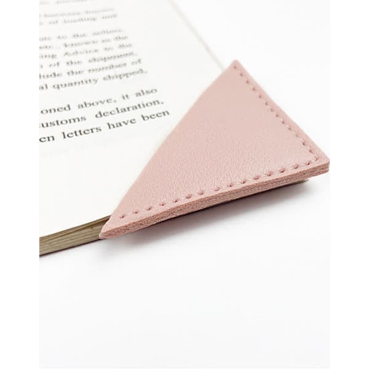 A pink PU leather corner bookmark rests on the edge of an open book, showcasing its triangular design.