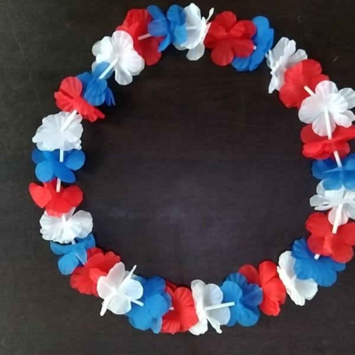 A circular Hawaiian lei featuring red, white, and blue flower petals, strung together for decoration.