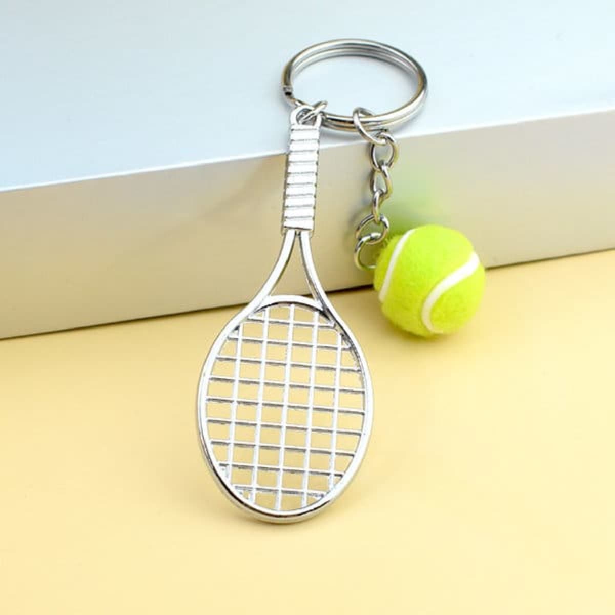A key ring featuring a silver tennis racket design and a small green tennis ball charm.