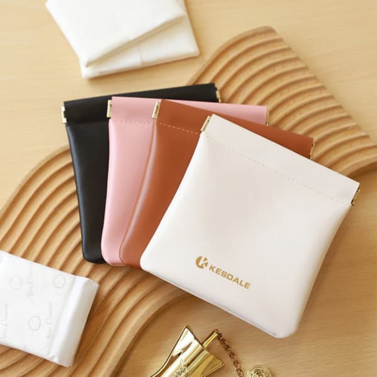 A set of four cosmetic bags in black, pink, tan, and cream, featuring a gold logo on one bag.
