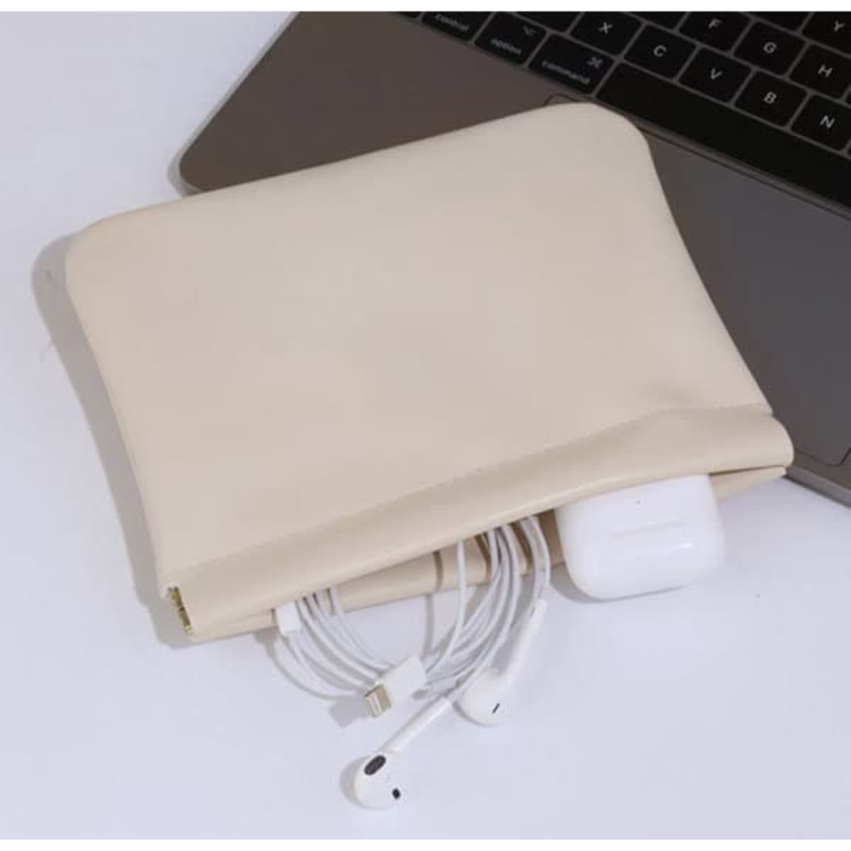 A small beige travel makeup bag is placed next to a laptop, containing wired earphones and a set of AirPods.