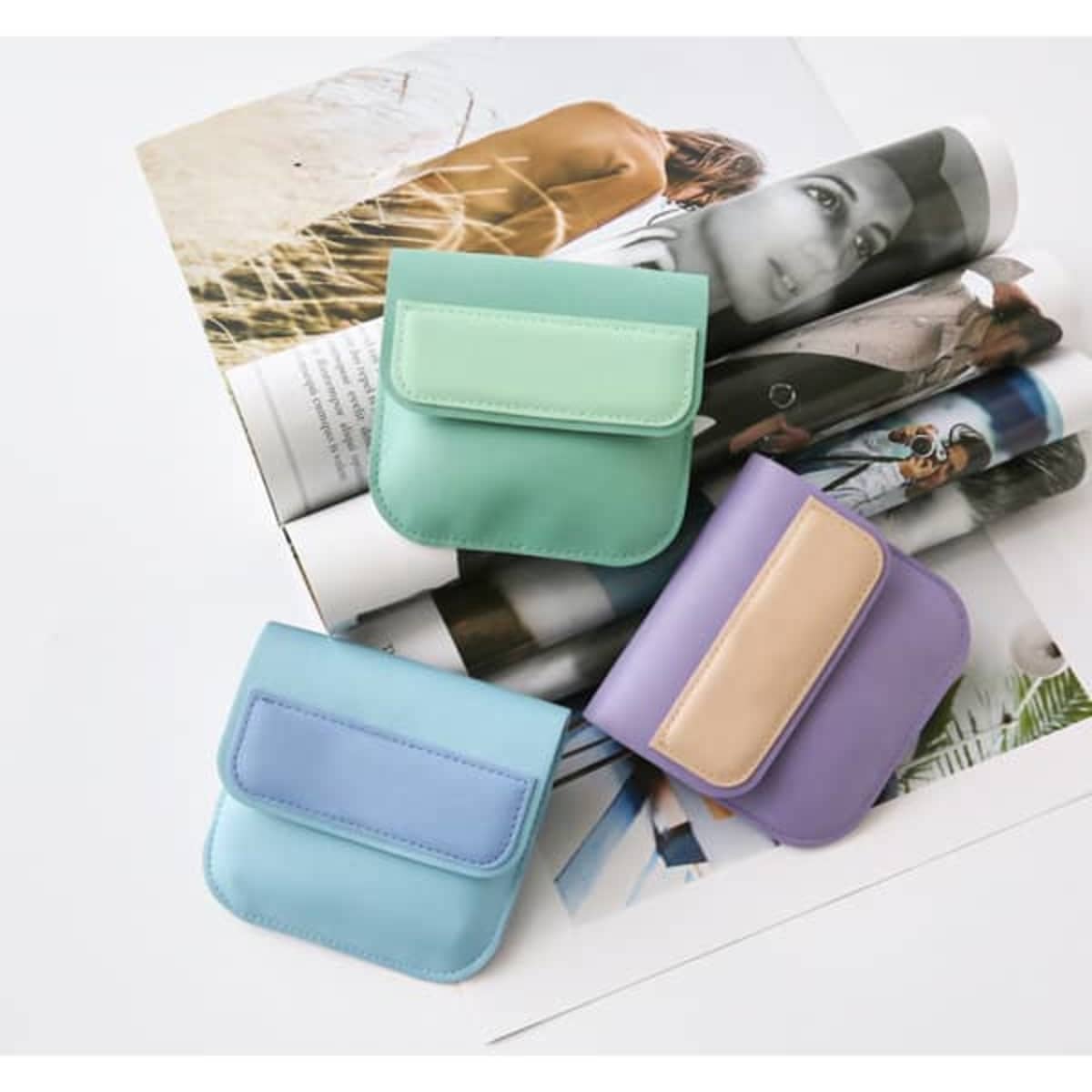 A set of three mini portable bags in mint green, light blue, and lavender, displayed on a magazine.