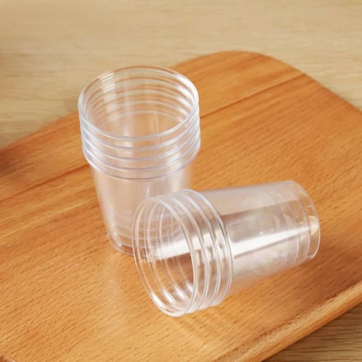 Clear disposable plastic party cups stacked on a wooden tray, showcasing their lightweight design.